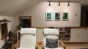 A living room with two wooden chairs, a wooden coffee table, a green and white striped rug, and a wall with three framed pictures.