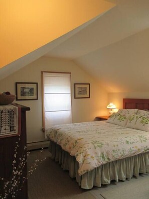 A bedroom with a sloped ceiling, a bed with floral bedding, a nightstand with a lamp, and two framed pictures on the wall. - Ithaca Urban Retreat II / Mid-term rental 30 days + only (Ithaca)