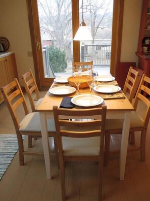 A dining area with a table set for six, wooden chairs, a chandelier, and a view through large windows. - Ithaca Urban Retreat II / Mid-term rental 30 days + only (Ithaca)