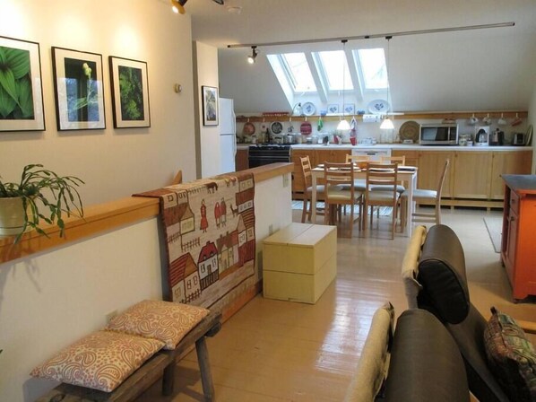 A cozy living room with a sofa, a bench, and a patterned rug. There is a kitchen in the background with a dining table and chairs. - Ithaca Urban Retreat II / Mid-term rental 30 days + only (Ithaca)