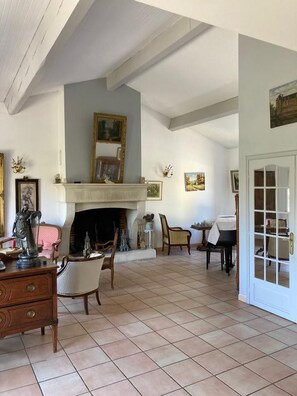 Een ruime woonkamer met een open haard, een grote spiegel en een deur naar een andere kamer.