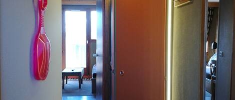 Un pasillo con una puerta de madera, un objeto rojo en la pared y un banco al fondo.