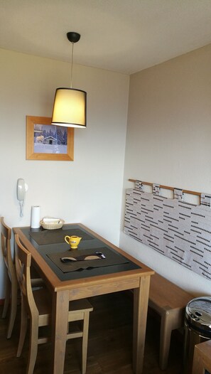 Un coin repas avec une table en bois, des chaises, une lampe, un tableau encadré, un téléphone fixé au mur et un tableau d’affichage.