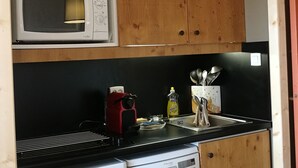 Eine kleine Küche mit Holzausstattung, einer Mikrowelle, einer Kaffeemaschine und einem Geschirrspüler.