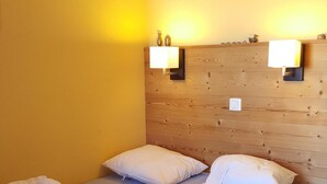 Ein Doppelbett mit weißen Bettbezügen, zwei Nachttischlampen und ein hölzernes Kopfteil in einem Zimmer mit gelben Wänden.