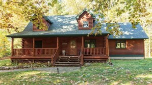 A log cabin with a porch, a small attached shed, and a stone foundation. - Secluded Torch Lake Cabin, 3BR, Sleeps 8, Firepit (Bellaire)