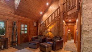 A spacious wooden cabin with a high ceiling, a staircase, leather sofas, and a stone wall. - Secluded Torch Lake Cabin, 3BR, Sleeps 8, Firepit (Bellaire)