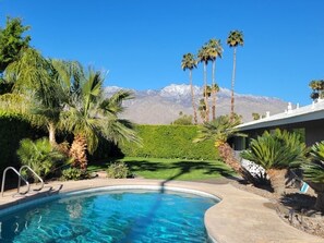 Ein Swimmingpool mit Bergblick, umgeben von Palmen und einem gepflegten Garten.