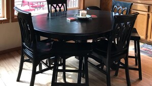A dining area with a round table and chairs, a window with a view of trees and an American flag, and wooden cabinets.