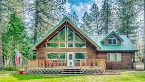 A two-story cabin with a green roof, a front porch, and a fenced yard.