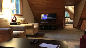 A cozy living room with a television, two armchairs, a coffee table, and a fireplace.