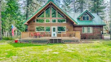 A two-story cabin with a green roof, a front porch, and a fenced yard.