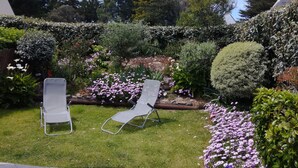 Un jardín con dos sillones de descanso, diversas plantas y un seto.