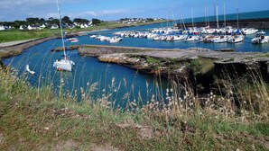 Una marina con barcos amarrados a lo largo de un canal estrecho, rodeada de zonas verdes y algunas casas al fondo.