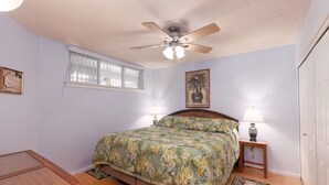 A bedroom with a bed, ceiling fan, bedside lamps, a window, and a small table. - Amazing Direct Ocean Front Condo - Beautiful Sunsets, watch dolphins and whales (Kailua-Kona)