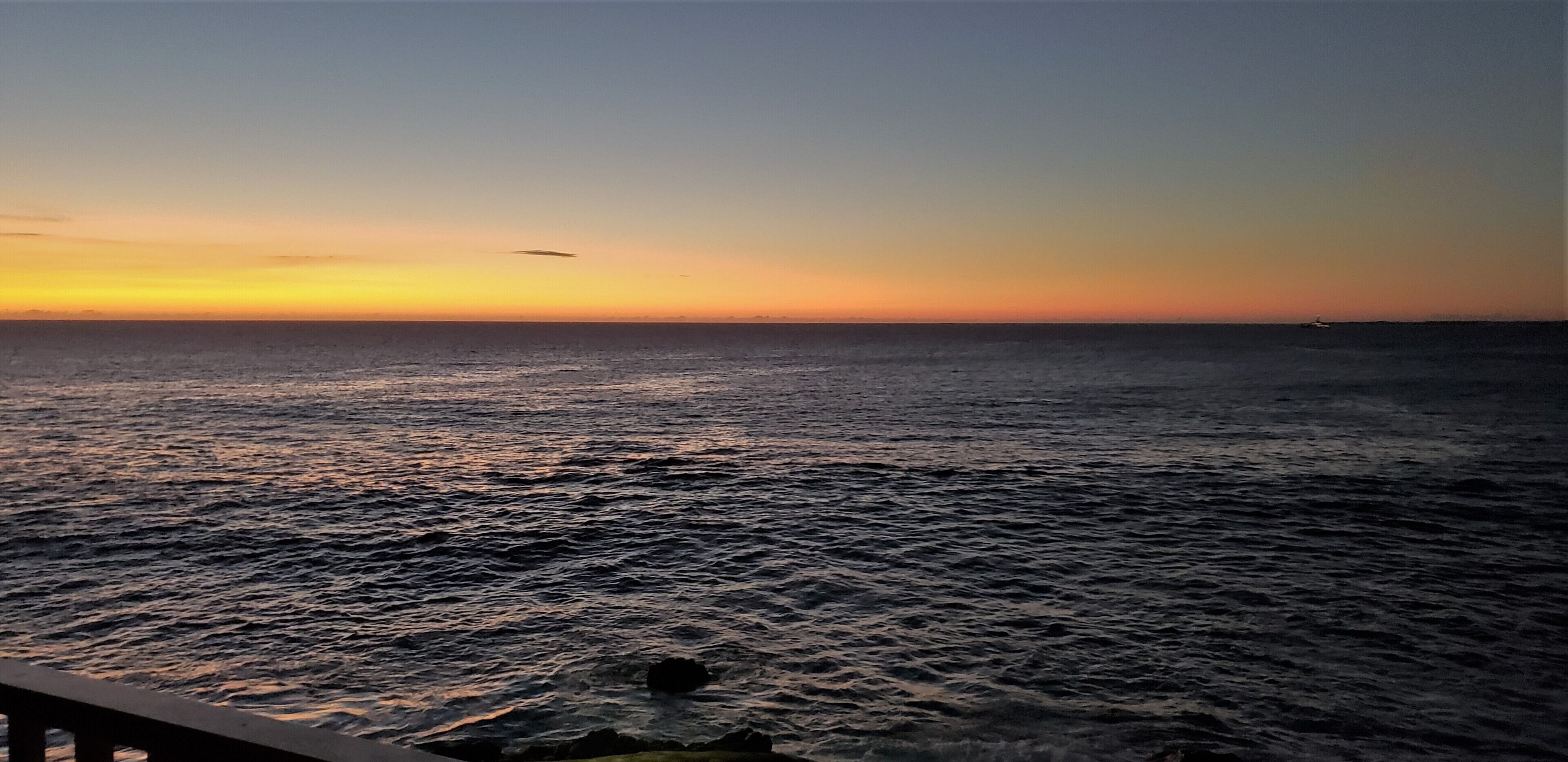 A view of the ocean at sunset with a wooden railing in the foreground.