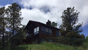 A two-story wooden cabin with a balcony, surrounded by tall pine trees and a grassy area. - Views for Days Mountain Retreat.  License#6025  (Estes Park)