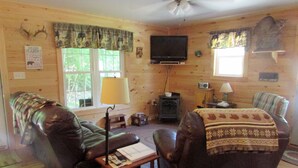 Un interior de cabaña con un sofá, un sillón y un televisor montado en la pared.
