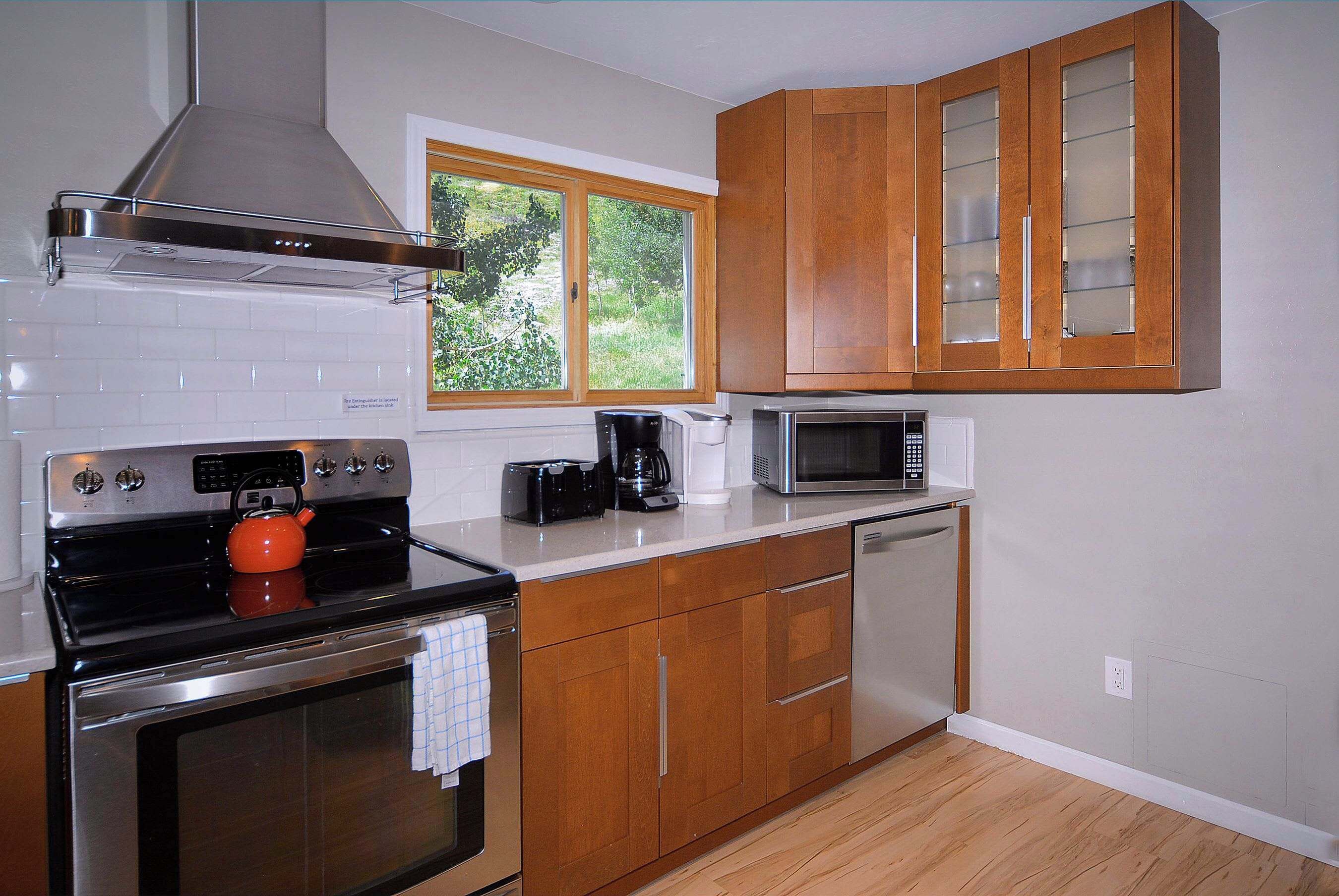 A kitchen with wooden cabinets, a stainless steel range hood, a microwave, a toaster, and a kettle.