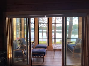 Una cabaña con puerta corredera de vidrio que da a una terraza con mobiliario exterior y vista al lago.