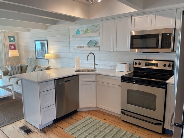 A modern kitchen with white cabinetry, a stainless steel dishwasher, a built-in oven, and a microwave. - Ocean Front, Sunrise Views, Well Appointed, Delaware Beach, Rehoboth By The Sea (Dewey Beach)