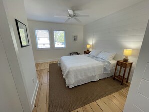 A bedroom with a bed, two bedside lamps, a ceiling fan, and a window with blinds.