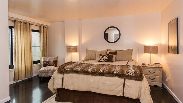 Une chambre avec un grand lit, deux tables de chevet, un miroir rond et une fenêtre avec des rideaux.
