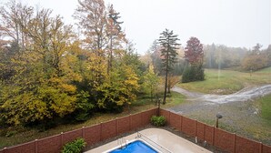 Une piscine bordée d’un mur en briques, avec vue sur des arbres et une zone herbeuse.
