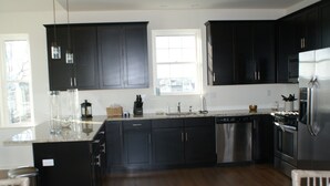 A modern kitchen with dark cabinetry, stainless steel appliances, and a large window providing natural light.