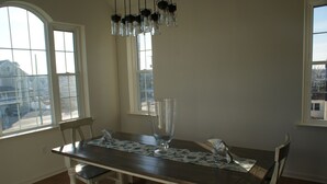 A dining area with a wooden table, chairs, a clear glass vase, and hanging light fixtures.