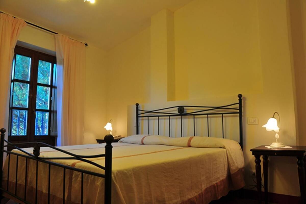 A bedroom with a bed, two bedside lamps, a window with curtains, and a nightstand.
