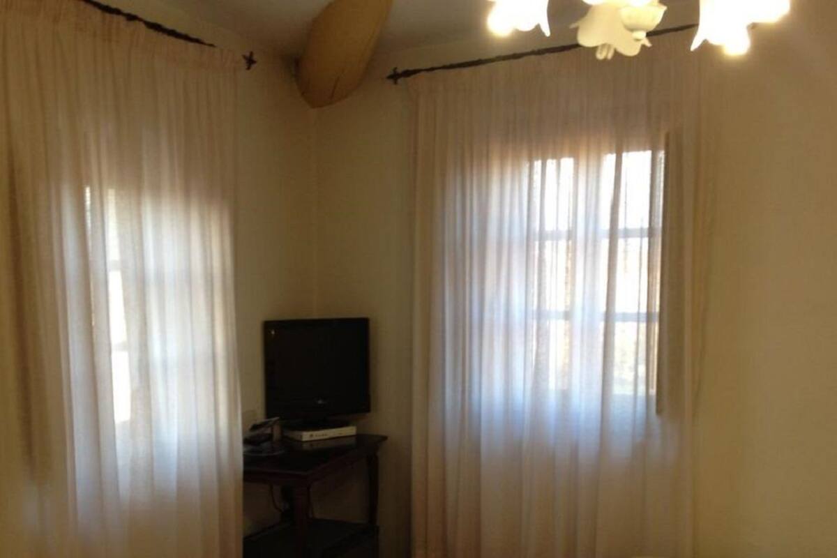 A room with two beds, a television on a stand, and a window with curtains.