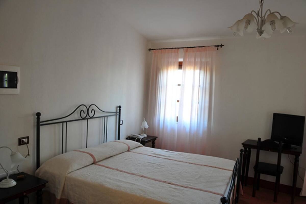 A bedroom with a bed, bedside table, lamp, TV, and curtains.