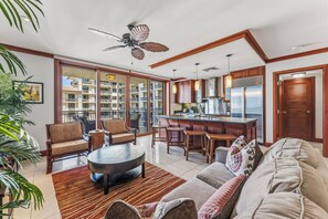 A spacious living area with a sofa, chairs, a coffee table, and a kitchen area with a bar. - Beach Villas at KoOlina Oceanviews (Kapolei)