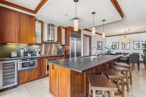 A modern kitchen with wooden cabinets, stainless steel appliances, and a central island with bar stools. - Beach Villas at KoOlina Oceanviews (Kapolei)