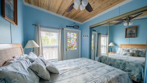 A bedroom with a bed, a ceiling fan, a window with blinds, and a door with a sign.