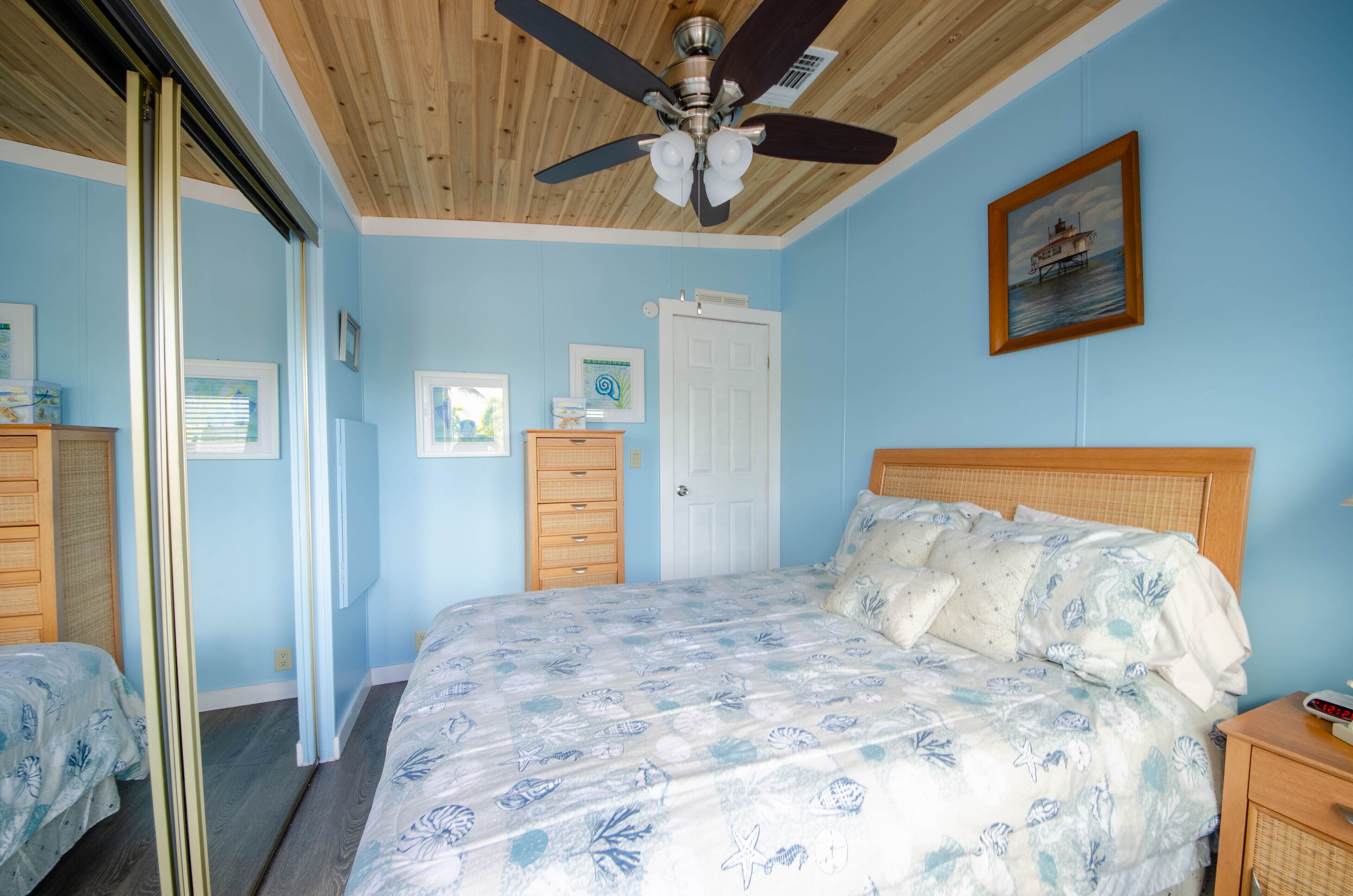 A bedroom with a bed, a ceiling fan, a door, and a framed picture on the wall.