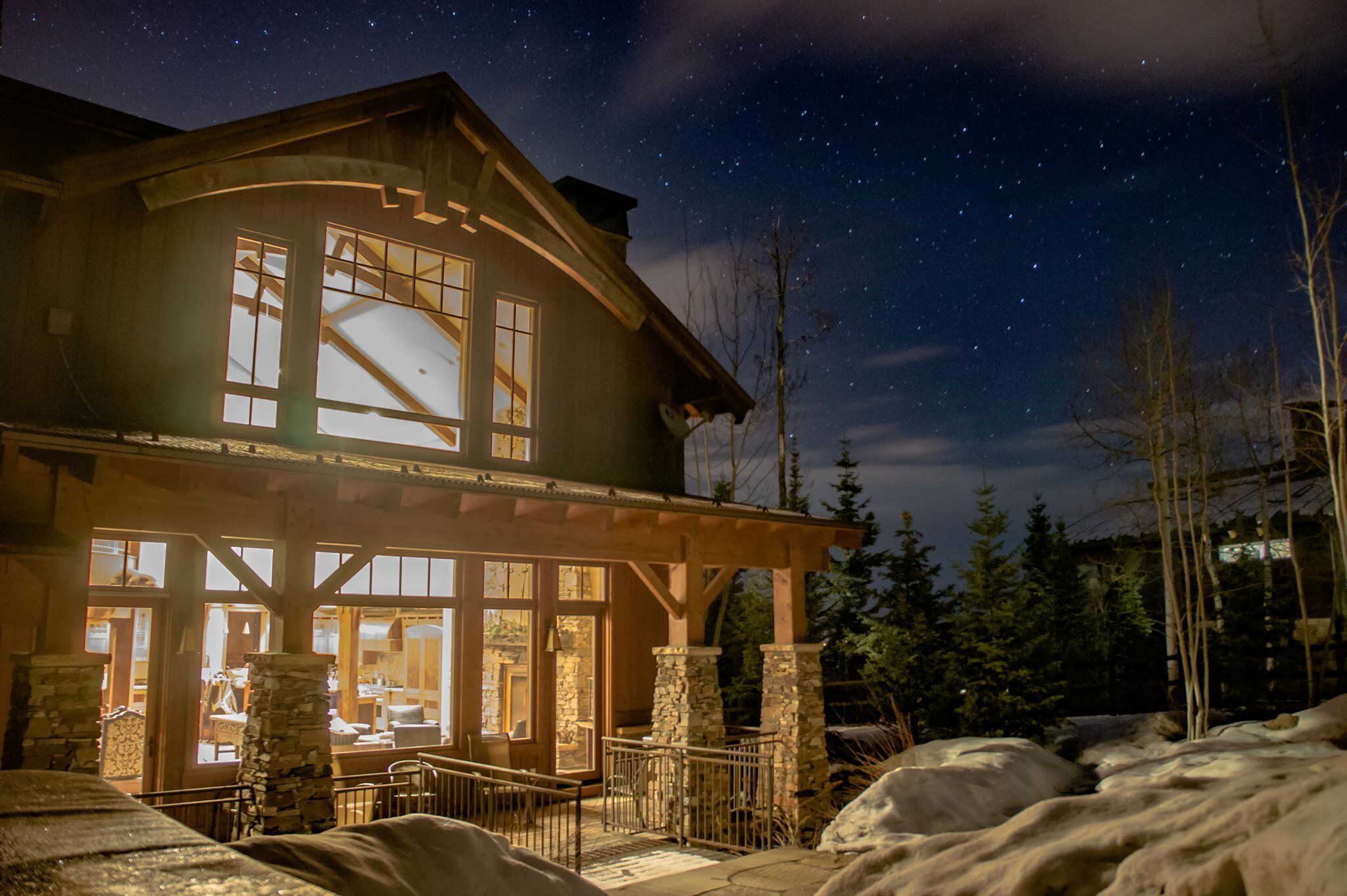 A lodge with a large window and stone pillars, surrounded by snow and trees.
