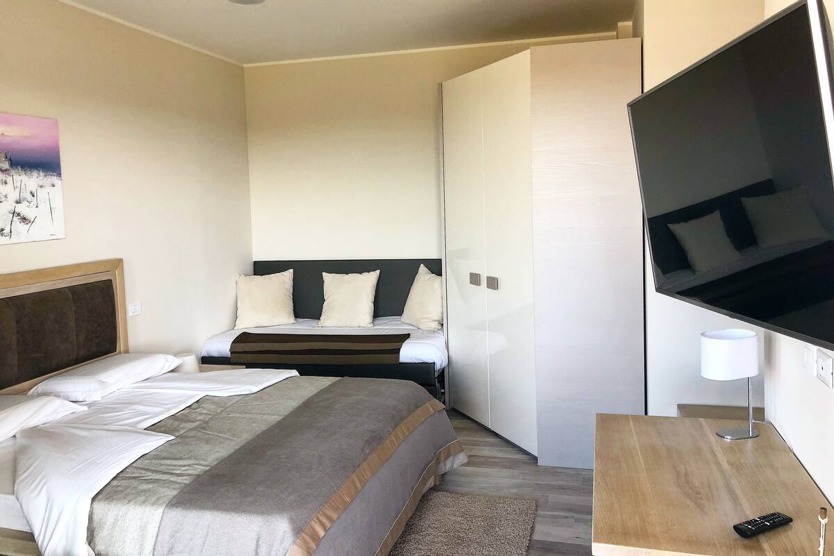 A hotel room with a bed, a TV, a bedside table, and a lamp.