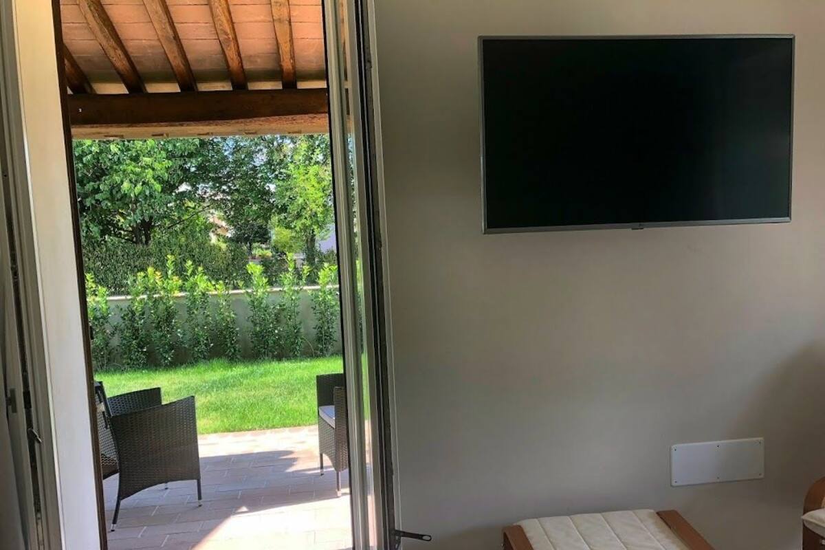 A room with a bed, a TV mounted on the wall, and a sliding glass door leading to a patio with outdoor furniture.