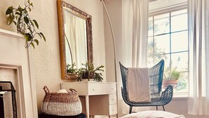 A cozy room with a vintage suitcase as a coffee table, a desk, a chair, and a large window with curtains. - Charming Midtown Home near Fairgrounds/TU/Downtown (Tulsa)