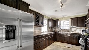 A modern kitchen with stainless steel appliances, dark wooden cabinets, and a large island. - Charming Midtown Home near Fairgrounds/TU/Downtown (Tulsa)