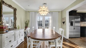 A dining room with a wooden table, white chairs, a large mirror, and a modern chandelier. - Charming Midtown Home near Fairgrounds/TU/Downtown (Tulsa)