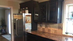 A kitchen with dark cabinets, a stainless steel refrigerator, and a tiled backsplash. - Charming Midtown Home near Fairgrounds/TU/Downtown (Tulsa)