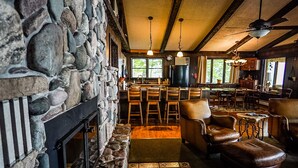 A stone fireplace, wooden bar stools, leather armchairs, and a dining area with a view of the outdoors. - Bigbay vacation home on Lake Independence. (Bigbay)