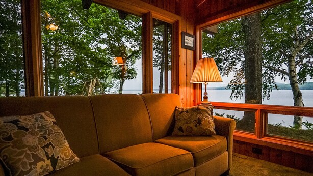 A cozy room with a sofa and a lamp, large windows with a view of trees and water. - Bigbay vacation home on Lake Independence. (Bigbay)