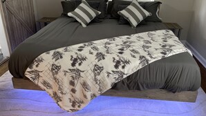 A bed with a floral-patterned blanket, two bedside tables, and a window with blinds. - The Masters Rental! Less than half a mile from course! (Augusta)