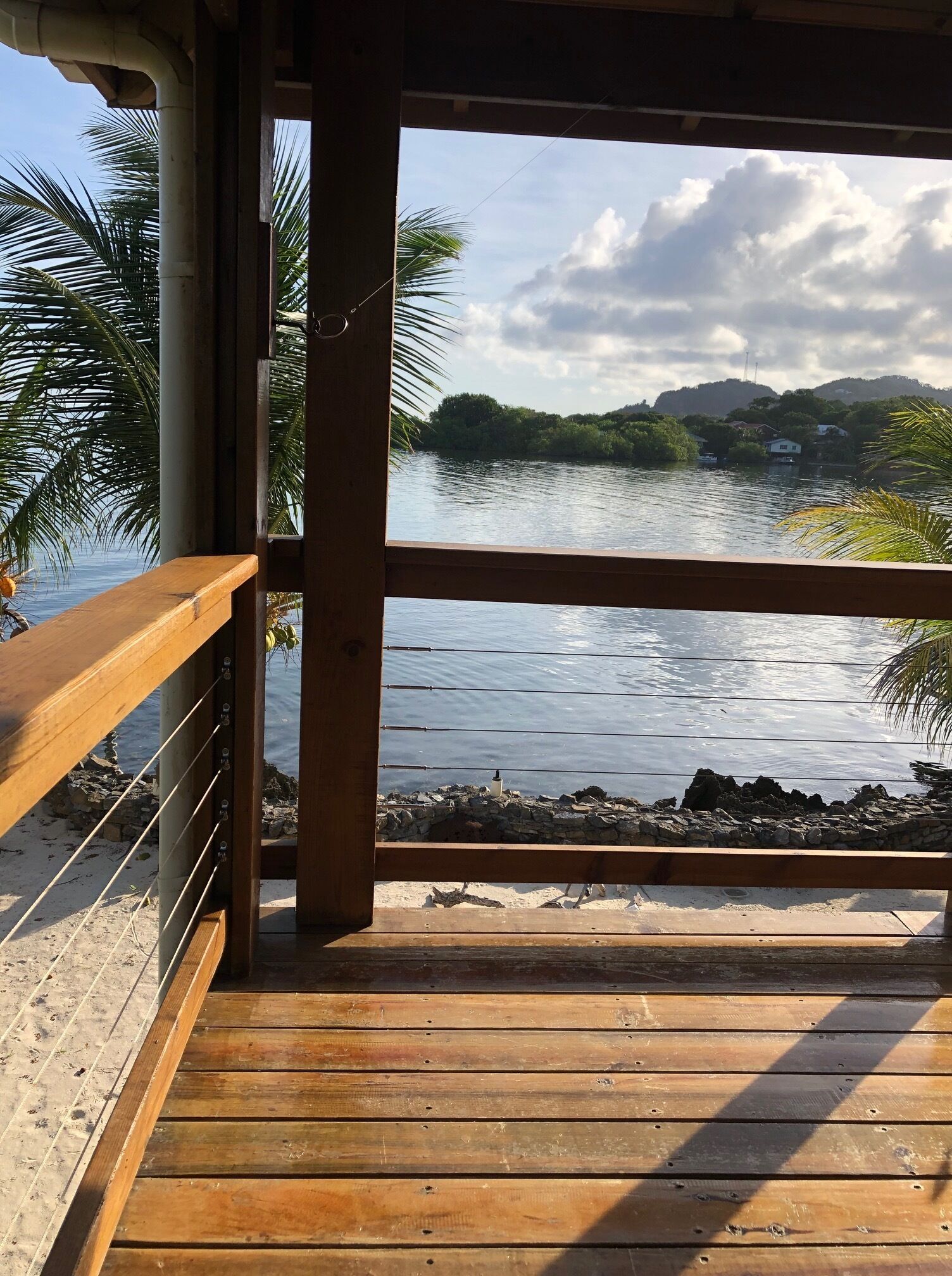 Una terraza de madera con vistas a un lago tranquilo, rodeada de vegetación y colinas.