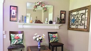 Une pièce comprenant deux chaises, une petite table avec un vase de fleurs, un miroir et un élément décoratif en métal accroché au mur.
