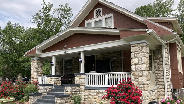 Une maison avec une façade en pierre, un porche à l’avant orné d’une balustrade blanche et le numéro « 2431 » au-dessus de la porte.
